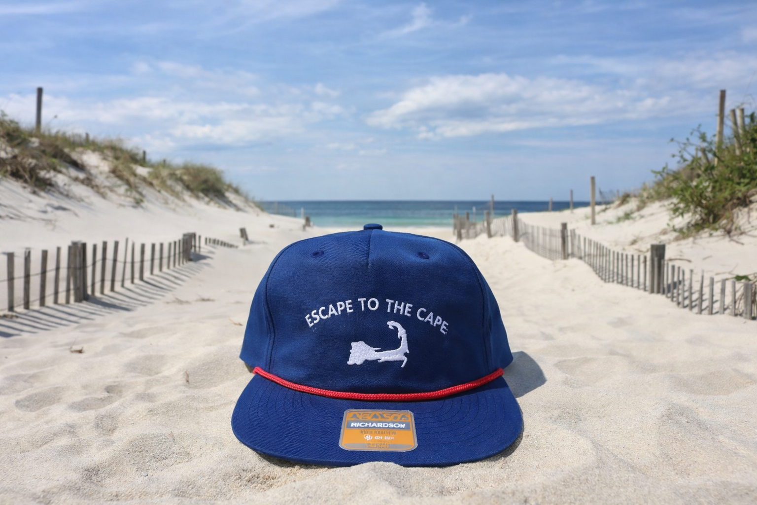 Blue cap with 'Escape to the Cape' text on a sandy beach