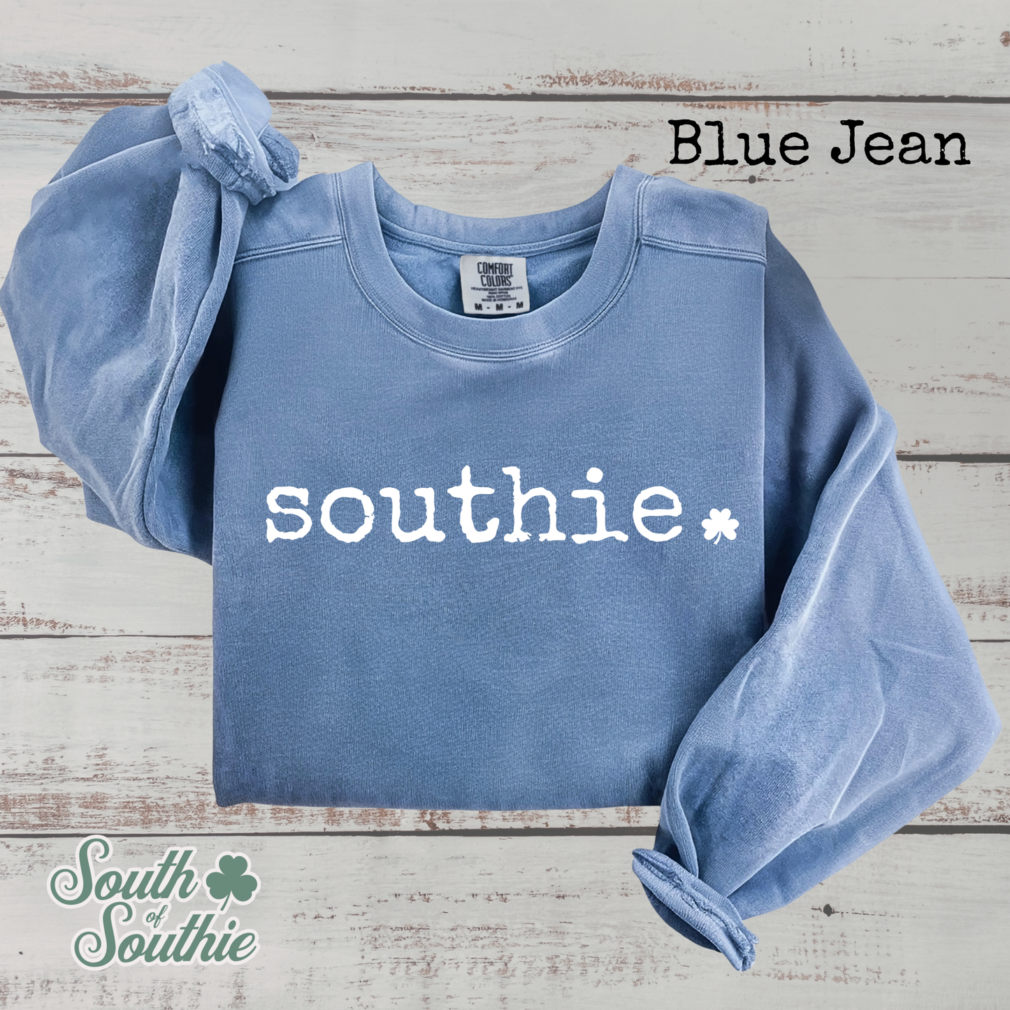 Blue sweatshirt with 'southie' text on a wooden surface, branded 'South of Southie'.