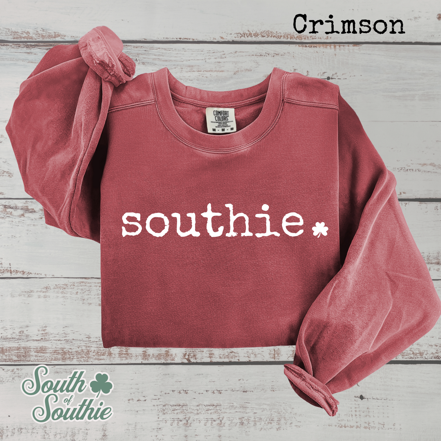 Red sweatshirt with 'southie' printed on it, on a wooden surface with 'South of Southie' branding.