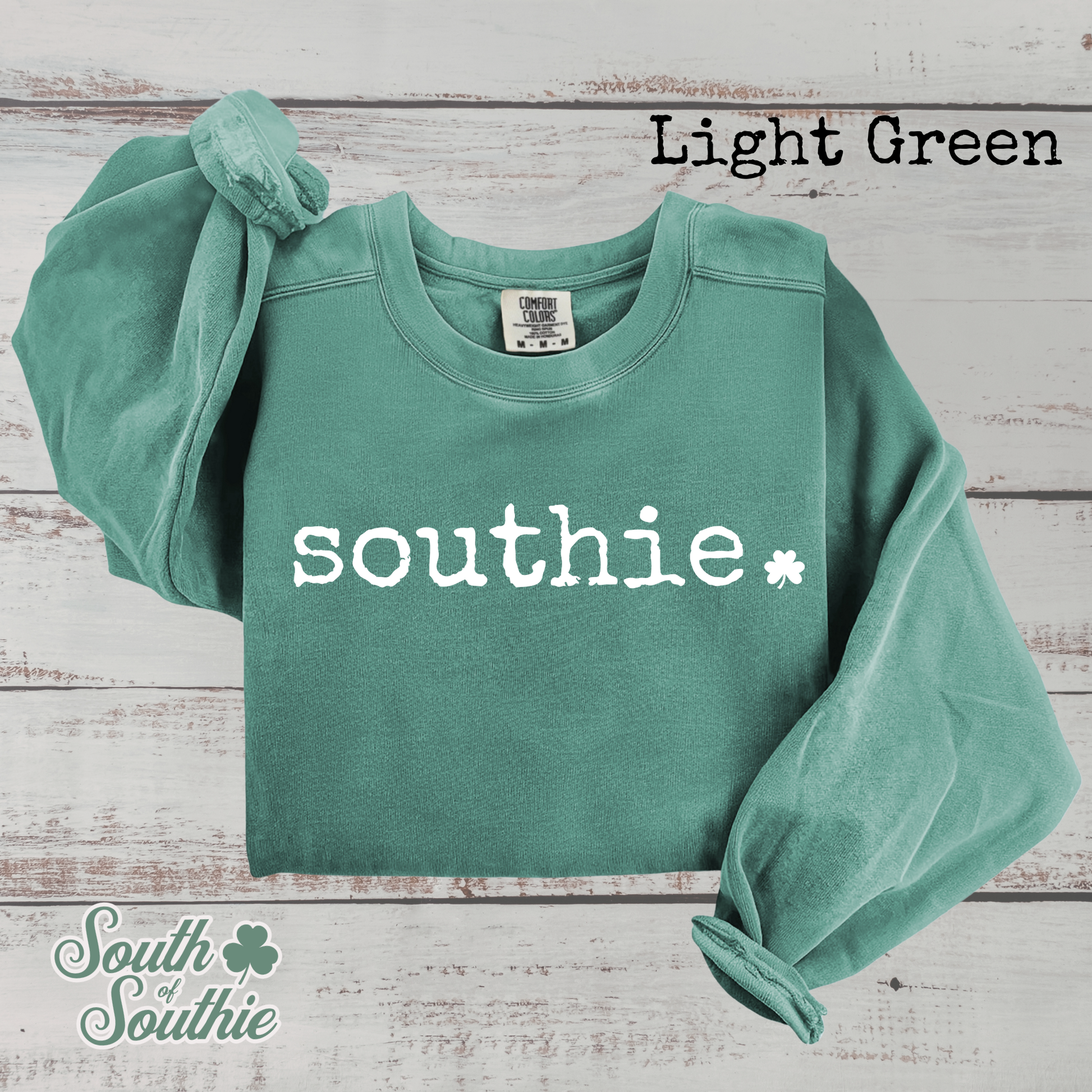 Light green sweatshirt with 'southie' print on a wooden surface, featuring the brand 'South of Southie'.